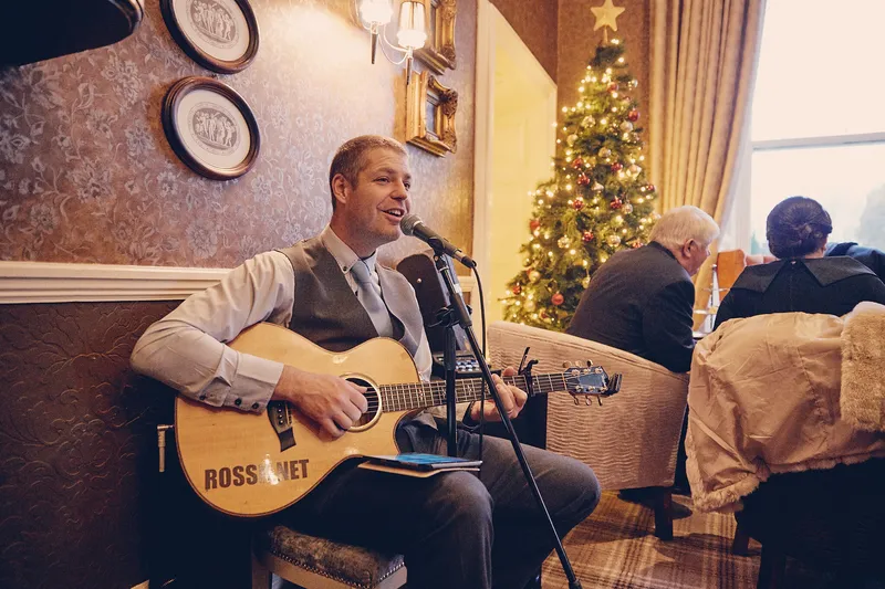 Een zanger met gitaar speelt bij de kerstboom tijdens de borrel