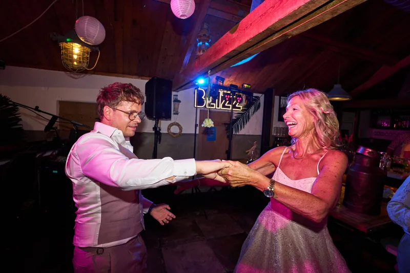 Een gast danst met een vrouw in een roze jurk, met het neonbord van Blizz erachter
