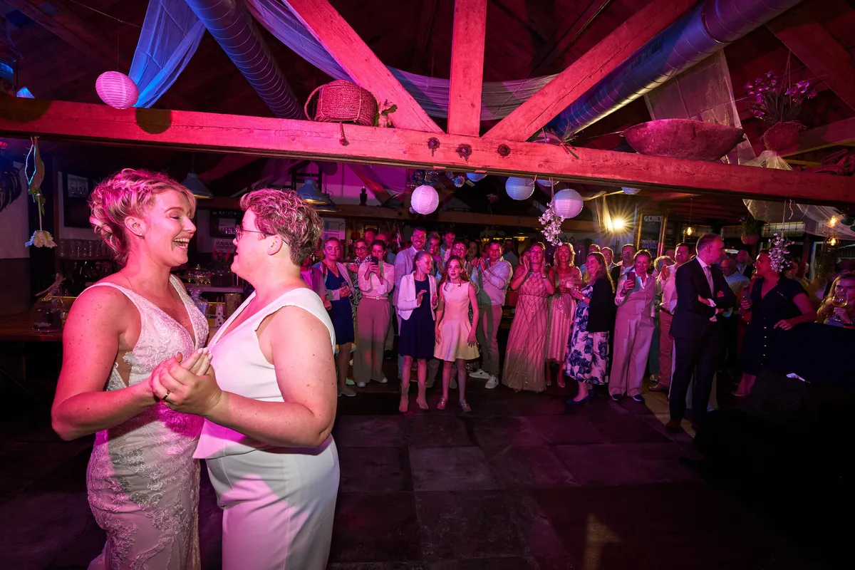Froukje en Mireille dansen hun openingsdans in roze licht, de gasten staan eromheen
