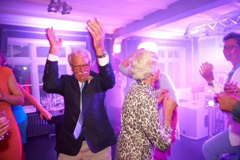 Een ouder stel danst met de armen omhoog in paars licht