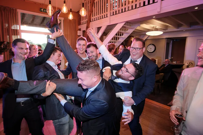 Gasten steken hun armen op in de houten zaal