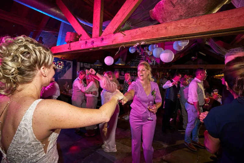 Een van de bruiden danst onder de houten balken in roze licht