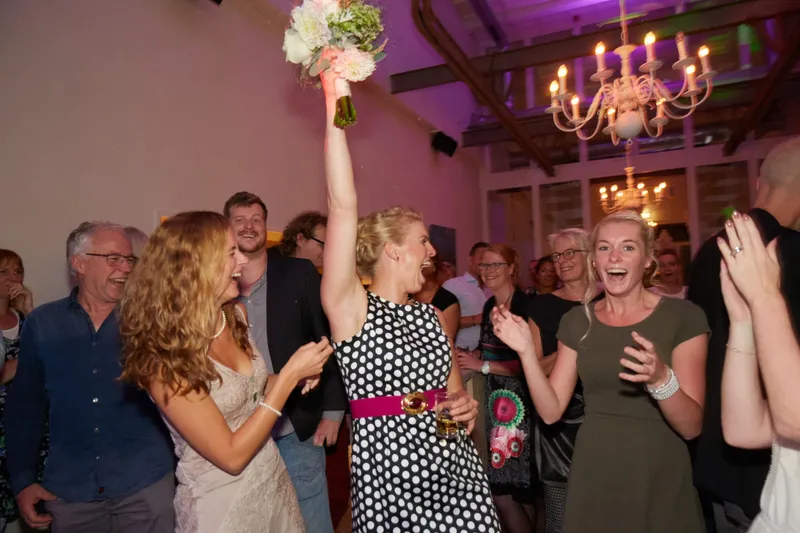 Akke steekt haar boeket hoog in de lucht tussen de dansende gasten