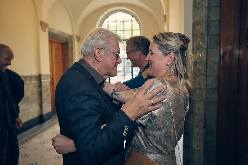 Jiska wordt omhelsd door een gast bij het raam in de gang