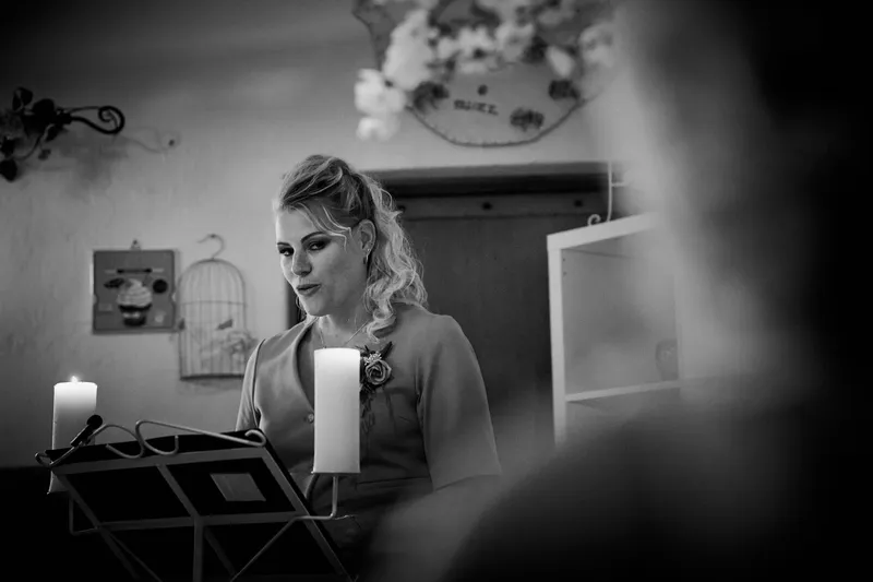 De ceremoniemeester, een vriendin van het stel, spreekt de bruiden toe bij de lessenaar, in zwart-wit