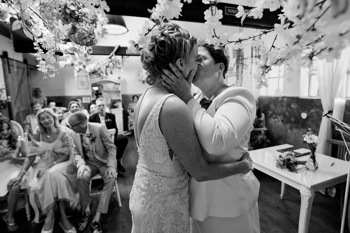 Froukje en Mireille kussen elkaar onder de bloesem, de gasten kijken toe