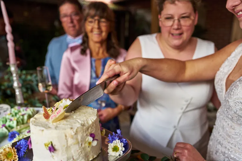 Froukje en Mireille snijden samen de taart met bloemen aan