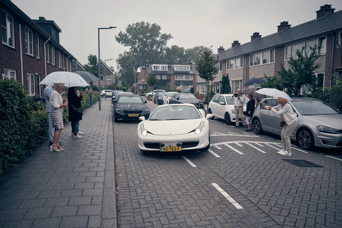 De witte Ferrari in de straat, buren met paraplu’s erlangs