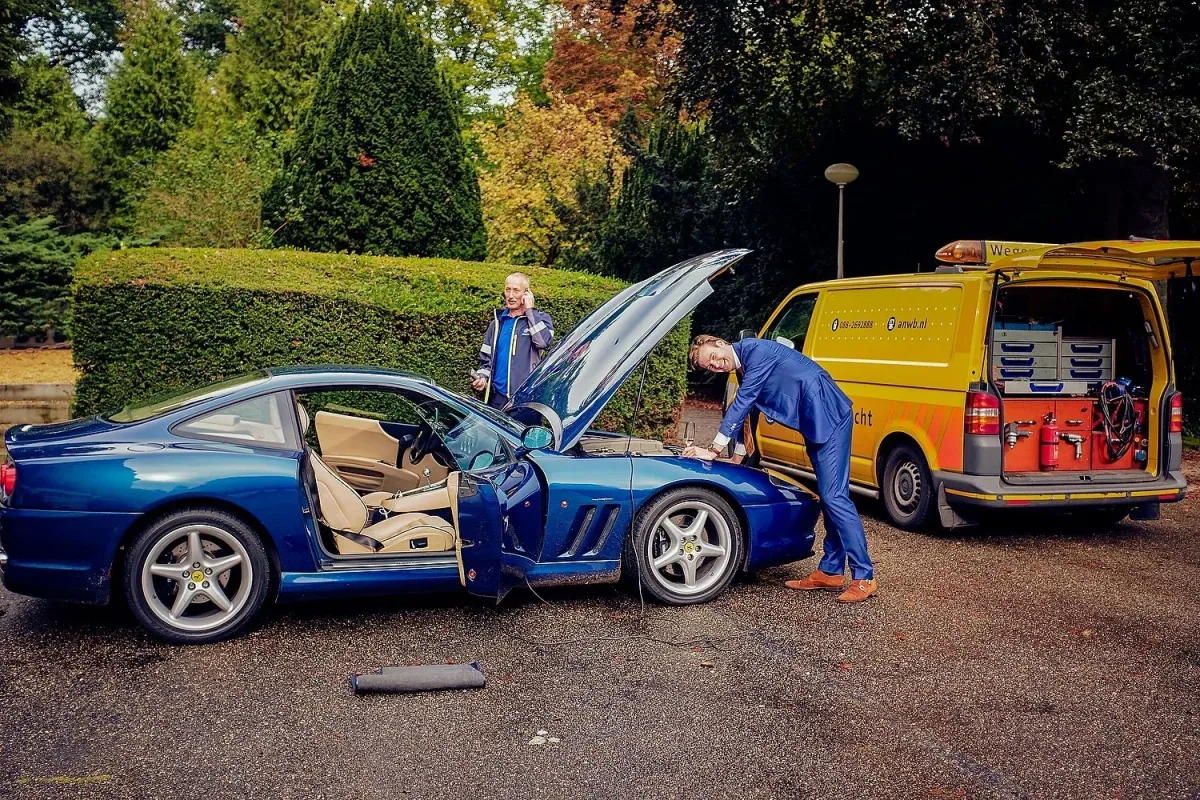 De bruidegom buigt over de open motorkap van een blauwe Ferrari, de wegenwacht probeert het alarm uit te zetten