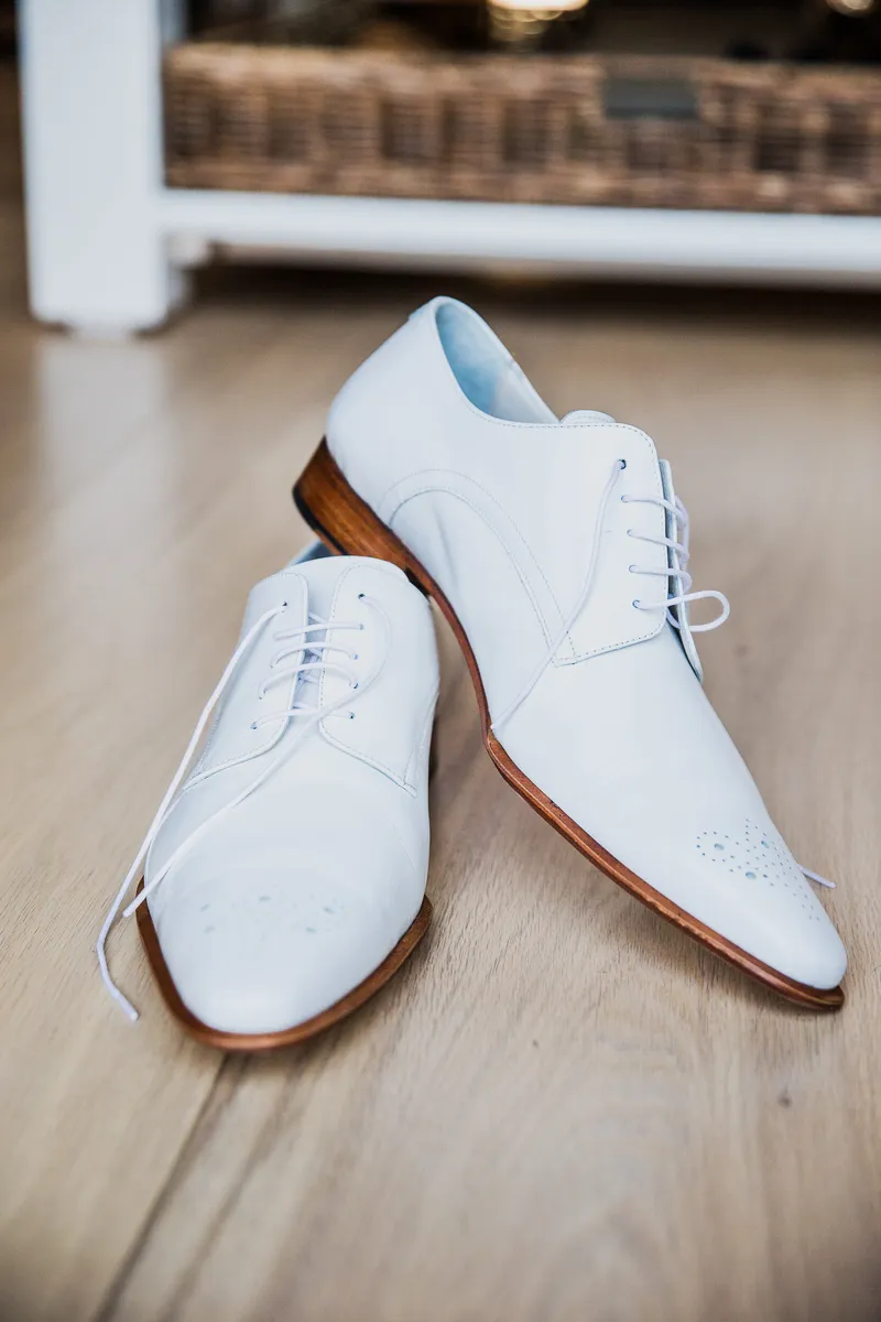 De witte schoenen met bruine zolen op de houten vloer