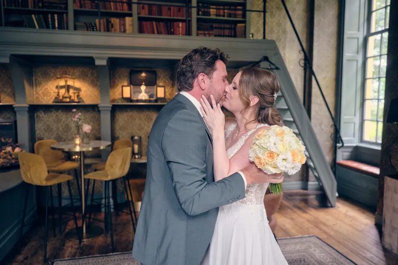 Fabian en Renée kussen elkaar tussen de boekenkasten