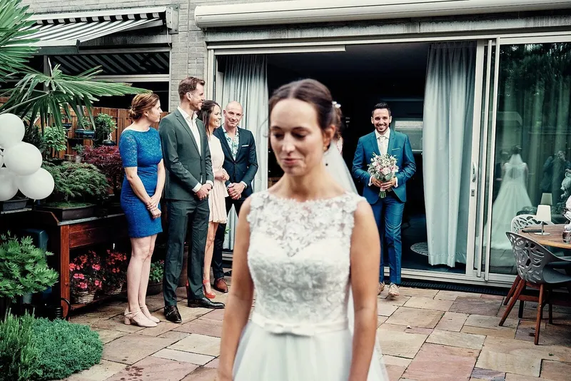 De bruid wacht op het terras terwijl de bruidegom met het boeket naar buiten komt