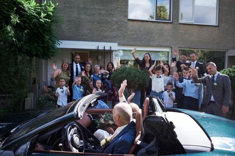 De familie zwaait het bruidspaar uit in de groene cabrio