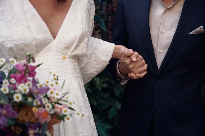 De handen van Anouk en Raphaël in elkaar, naast het boeket