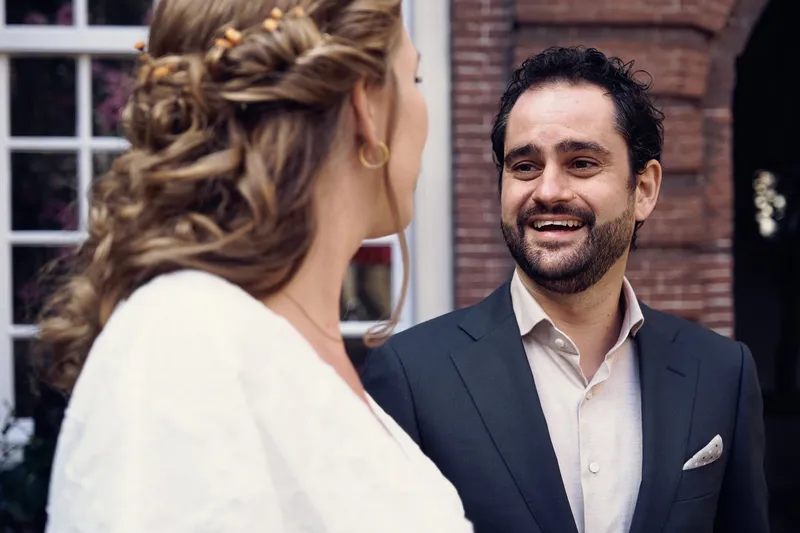 Raphaël lacht naar Anouk, vlak bij de bakstenen gevel