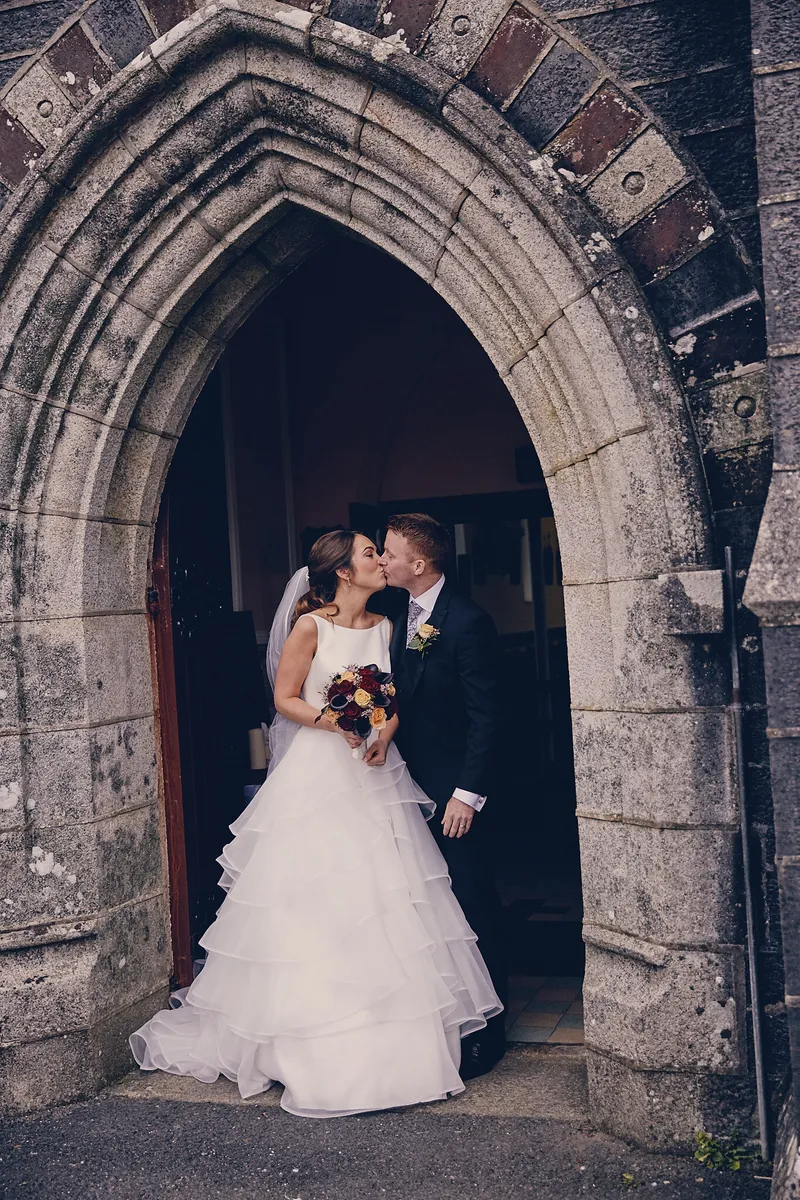 Shane en Caitriona kussen in de stenen boog van de kerkdeur