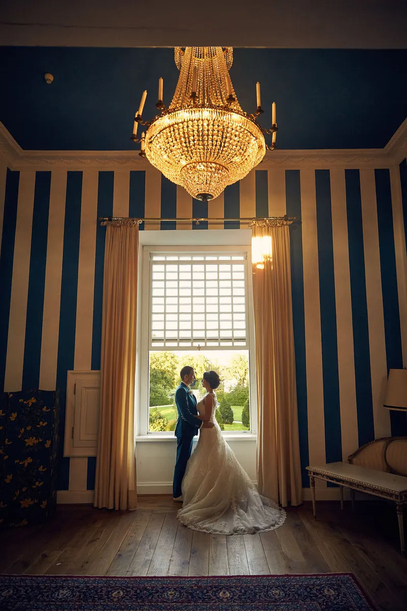 Bart en Frederike bij het hoge raam onder de kroonluchter in het kasteel