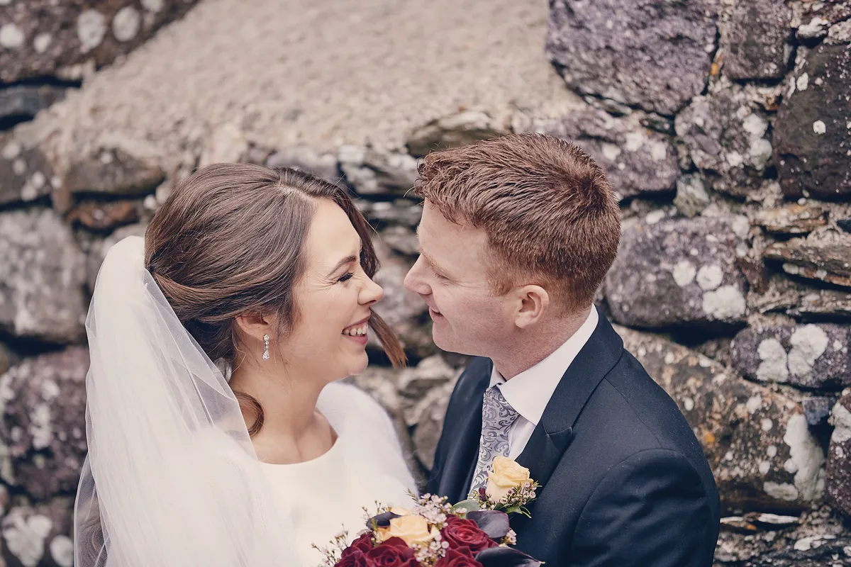 Caitriona en Shane lachen naar elkaar bij de stenen muur