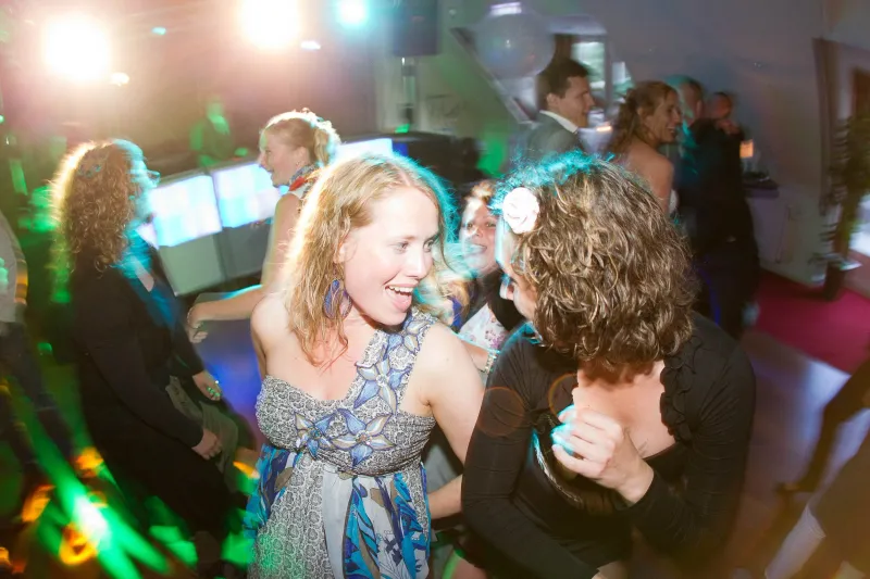 Gasten dansen in gekleurd licht, een vrouw lacht breed naar de camera