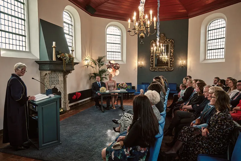 De trouwzaal met kroonluchters en de gasten op blauwe stoelen