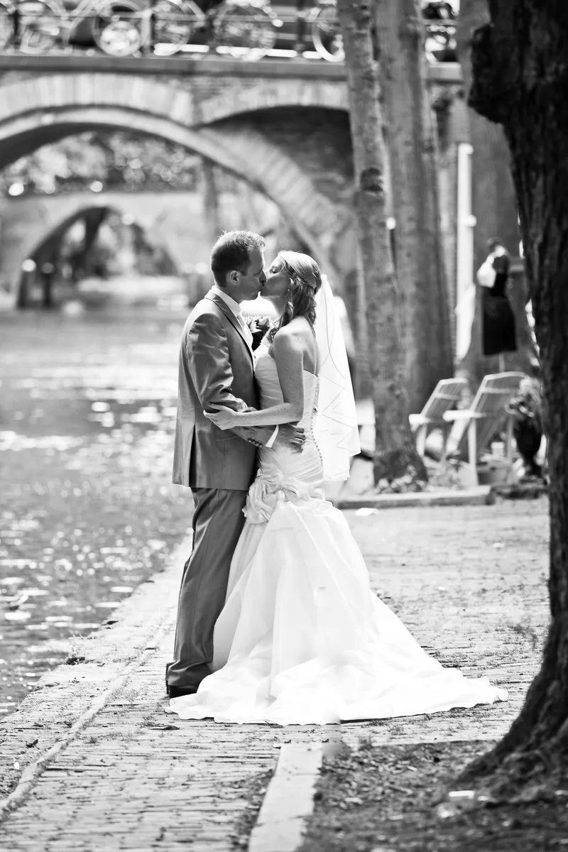 Loes en Jan kussen bij de gracht, met een brug op de achtergrond, in zwart-wit