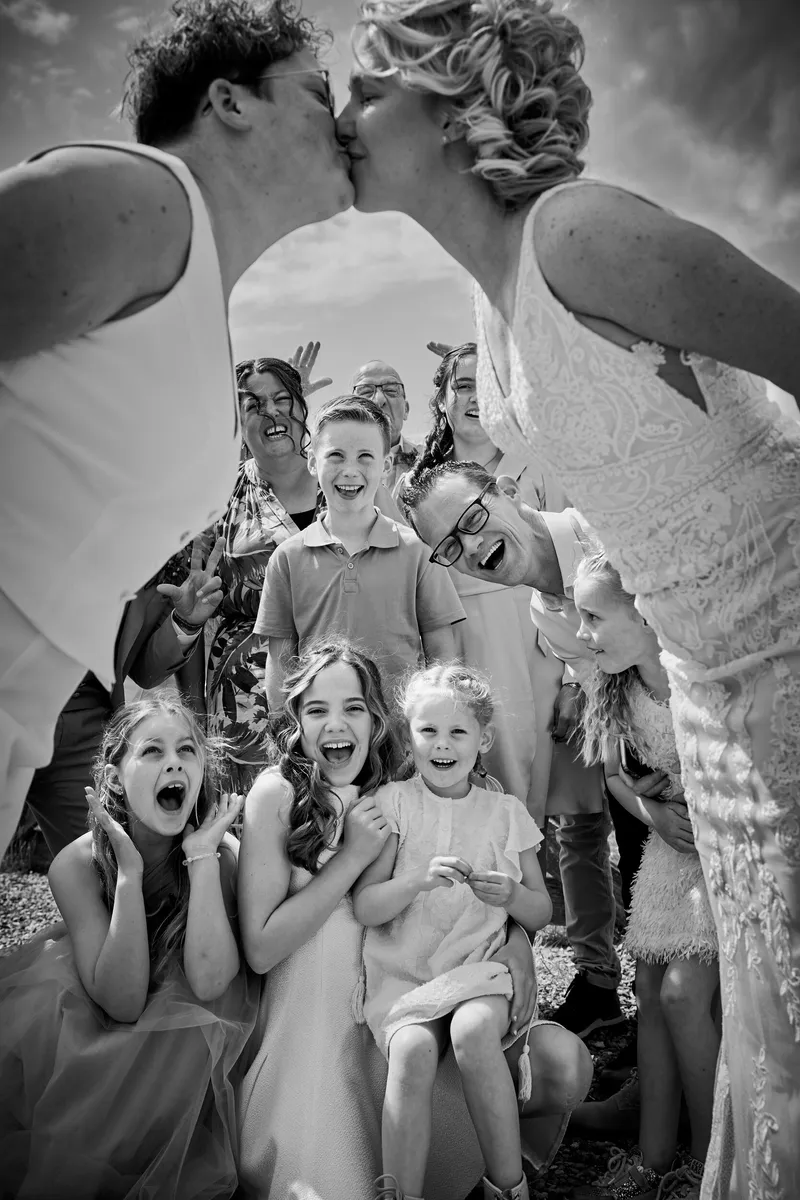De bruiden kussen elkaar, de kinderen eronder gillen en lachen, in zwart-wit