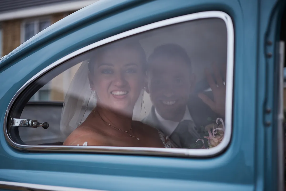 Liëla en Jeffrey lachen door het raam van de blauwe oldtimer