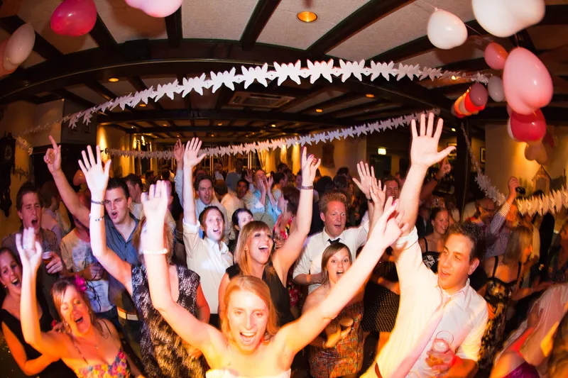 Gasten dansen met de armen omhoog onder de ballonnen, Loes in het midden