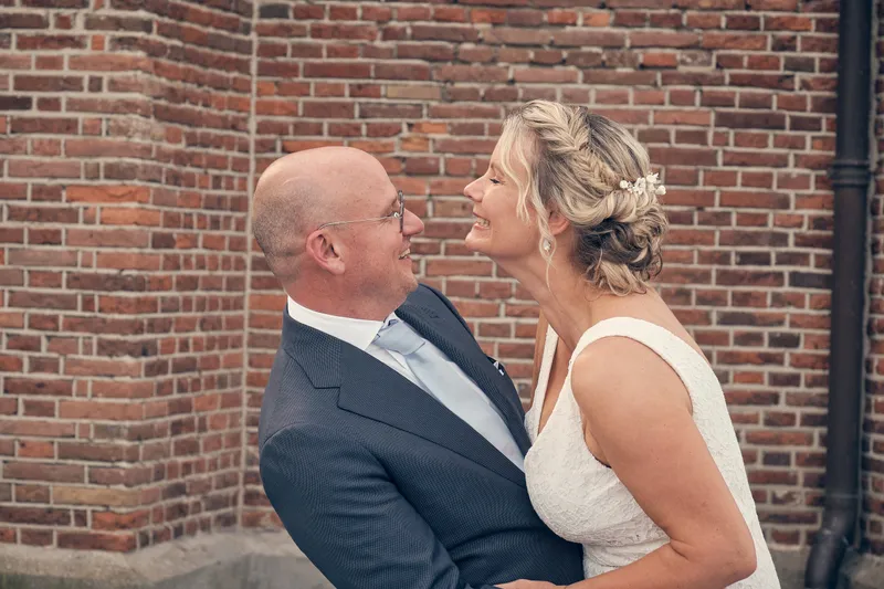 Bram en Elles omarmen elkaar tegen de bakstenen muur van de kerk