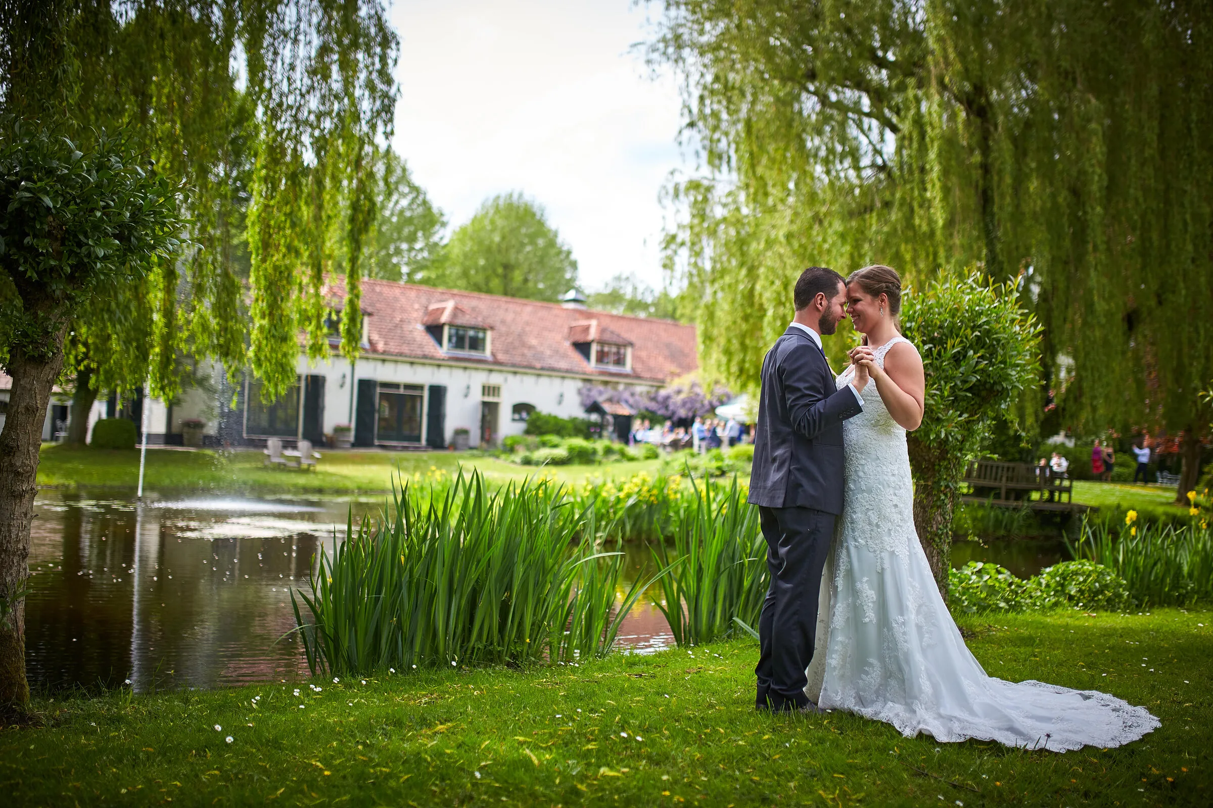 Robbert en Nadine lopen langs de vijver bij Het Land van Belofte, met het witte huis en de wilgen erachter