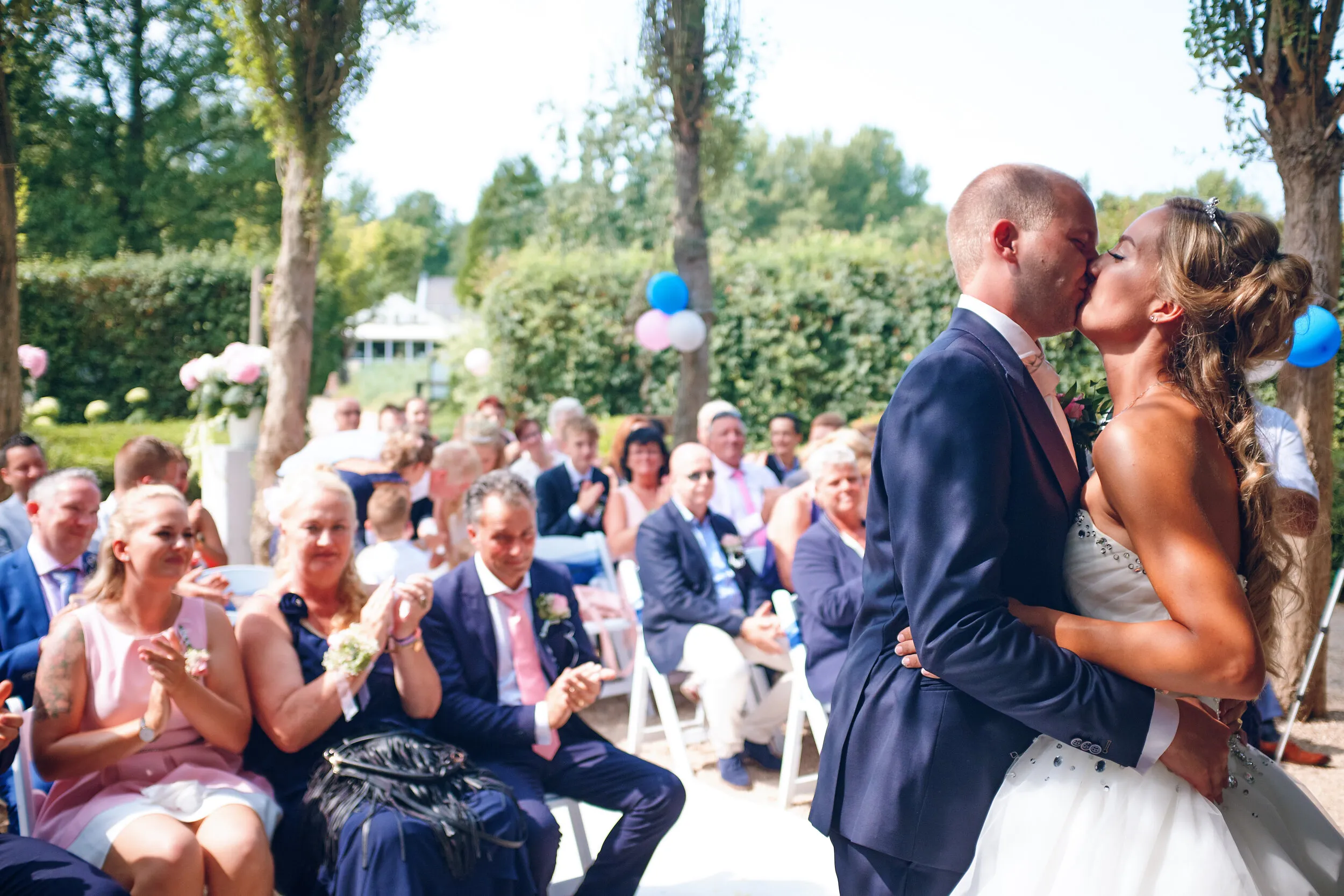 Kevin en Marcella kussen elkaar tijdens de ceremonie buiten bij Vida, de gasten kijken toe