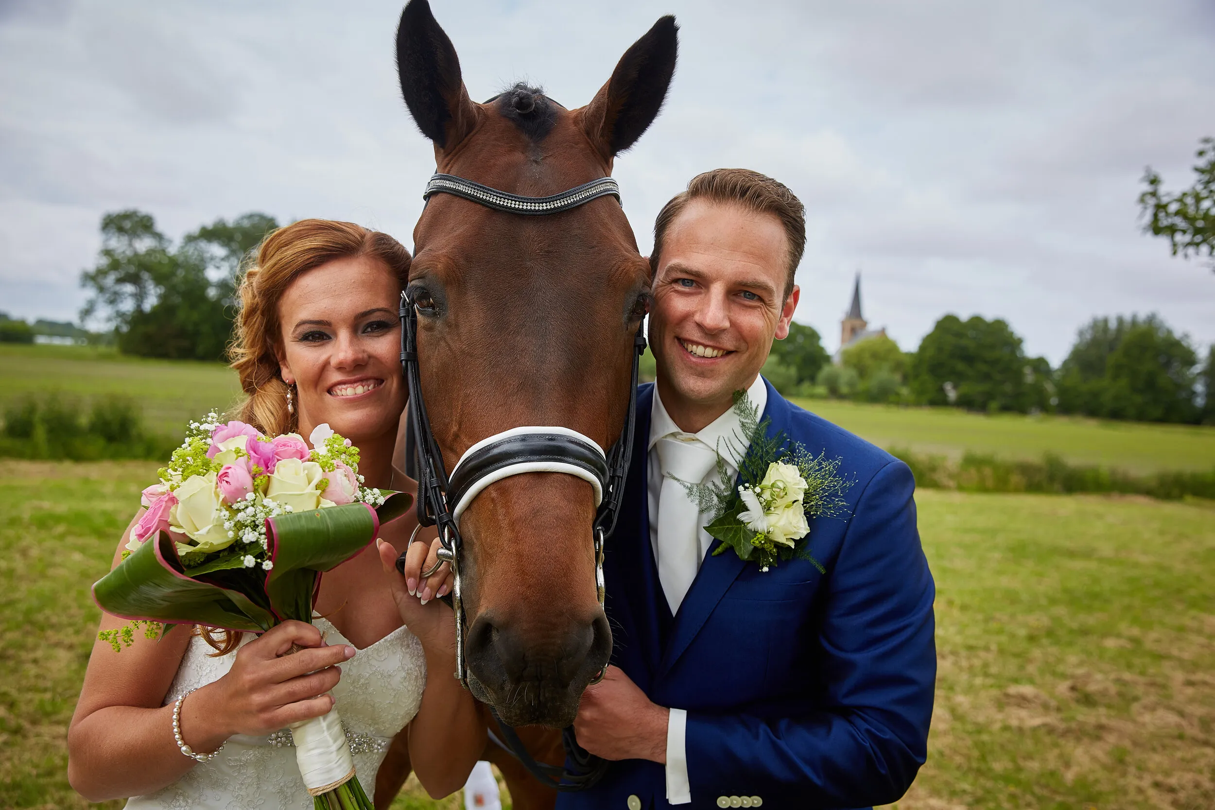 Trudy en Ron met het paard van Trudy in de wei, met een kerktoren in de verte