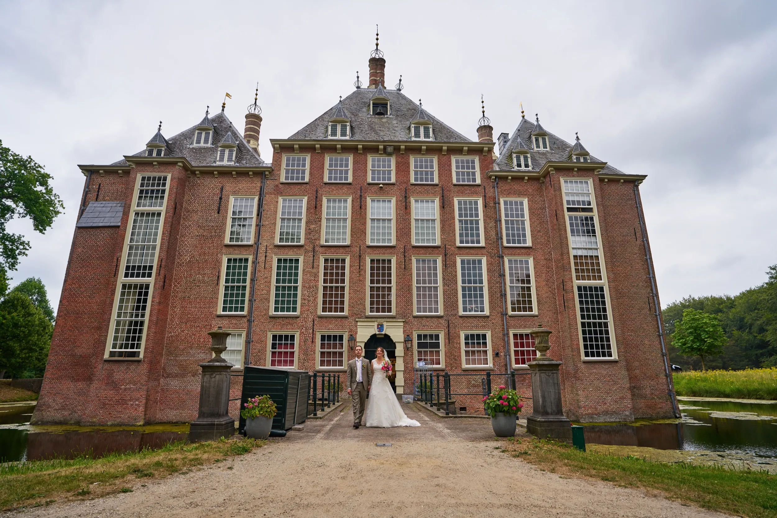 Een bruidspaar klein op het pad voor Kasteel Duivenvoorde, het kasteel symmetrisch in beeld
