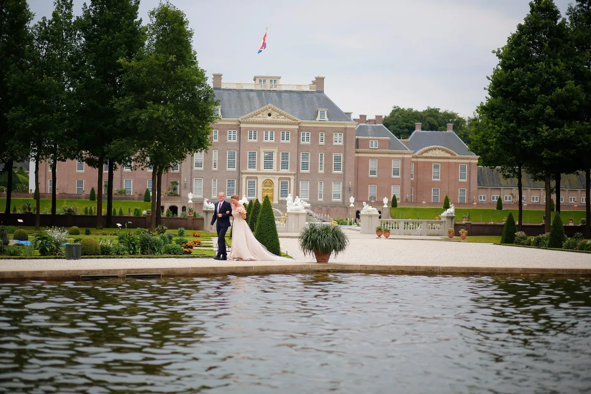 De stoet loopt door de tuin, gezien over het water