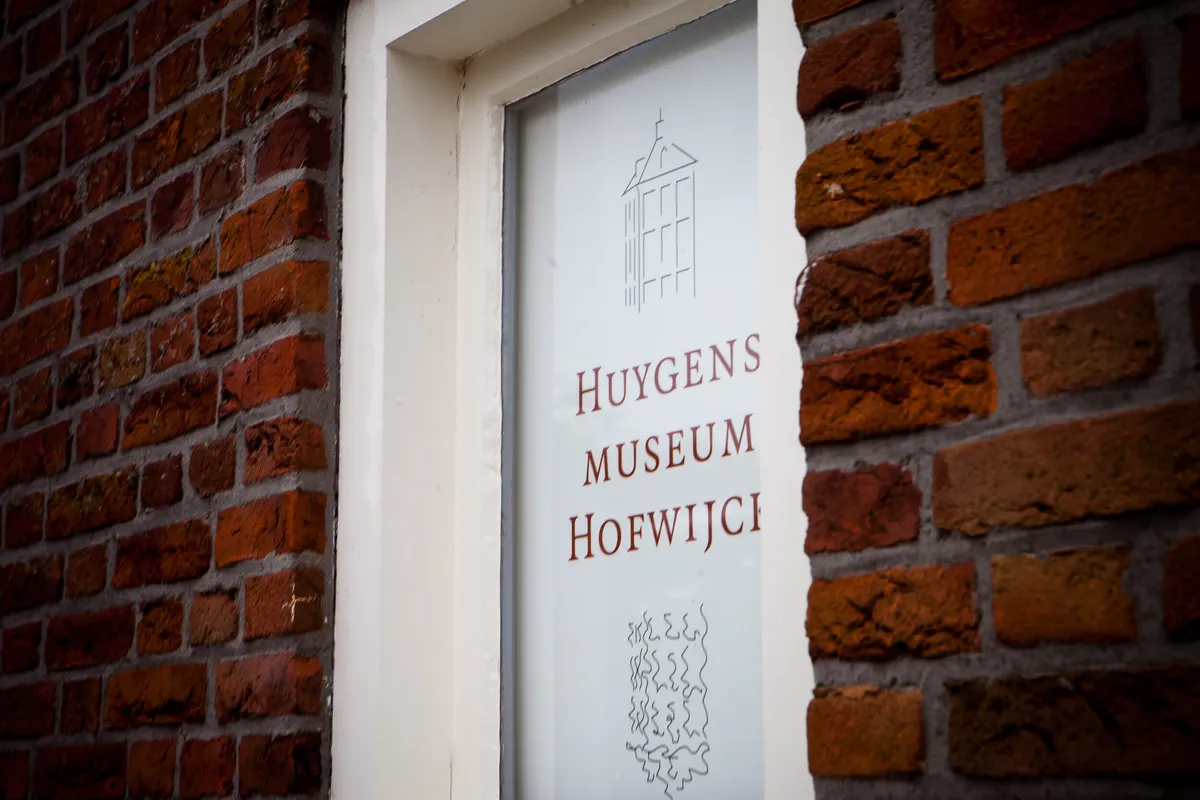 Het bord van Huygens Museum Hofwijck op de bakstenen muur