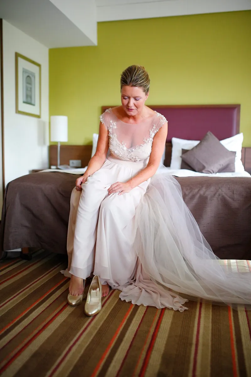 Jaqueline zit op het bed in haar trouwjurk