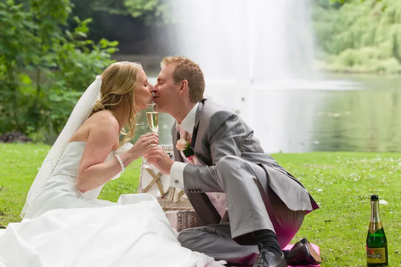 Loes en Jan kussen met een glas champagne bij de vijver in het Julianapark