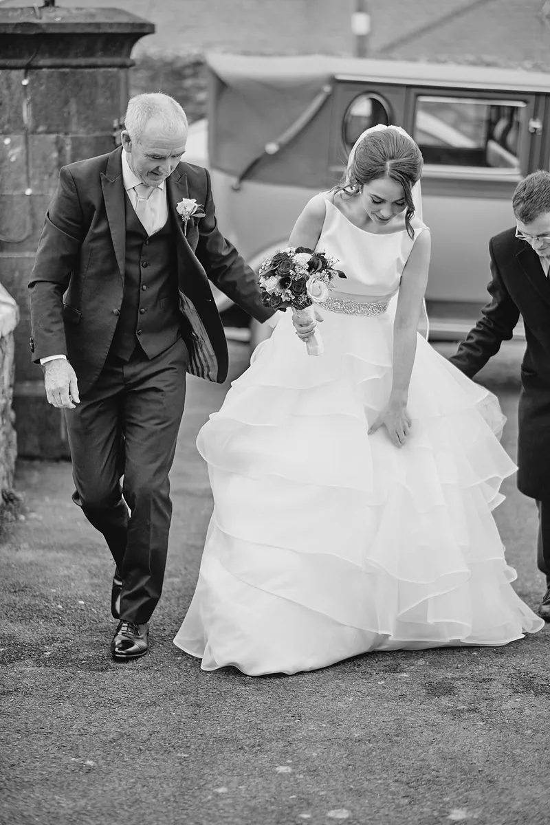 Caitriona stapt met haar vader uit de oldtimer, in zwart-wit