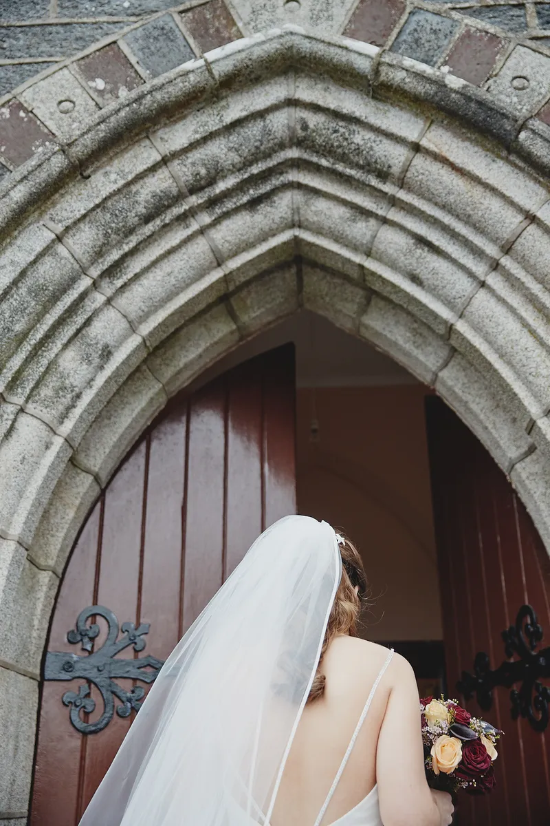 Caitriona onder de stenen boog van de kerkdeur
