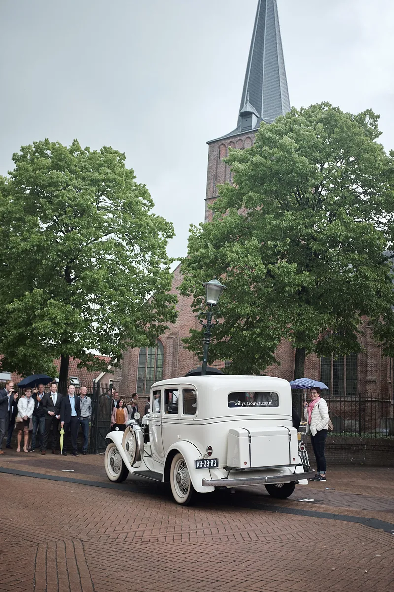 De oldtimer voor de kerk, met gasten onder paraplu’s