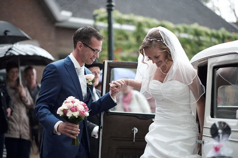 Femke en Arjan stappen uit bij de kerk, gasten met paraplu’s