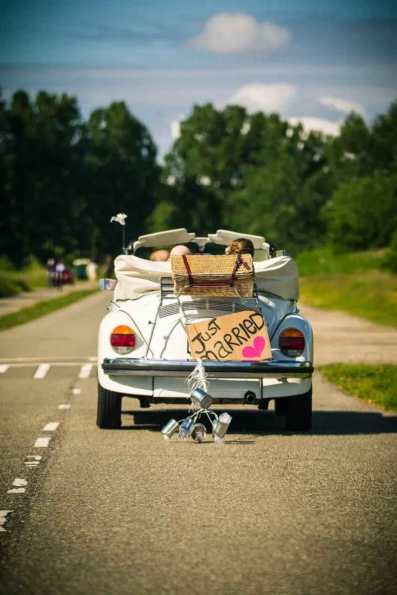 Witte Volkswagen Kever cabrio met mand, ‘Just Married’-bord en blikjes op een landweg