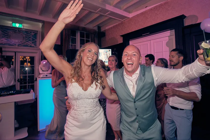 Het bruidspaar danst met de armen omhoog op de dansvloer