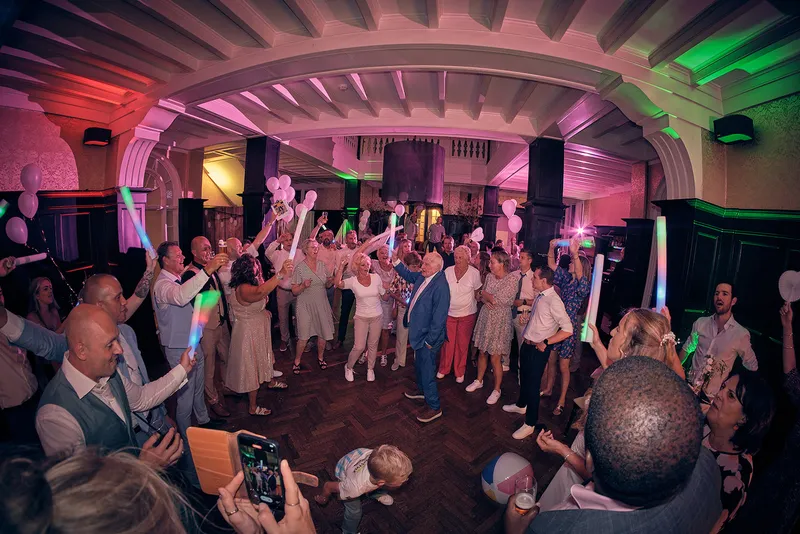 De volle dansvloer met glowsticks, het bruidspaar midden tussen de gasten
