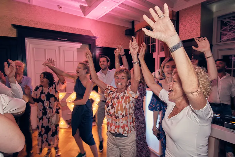 Gasten dansen met de armen hoog in roze licht