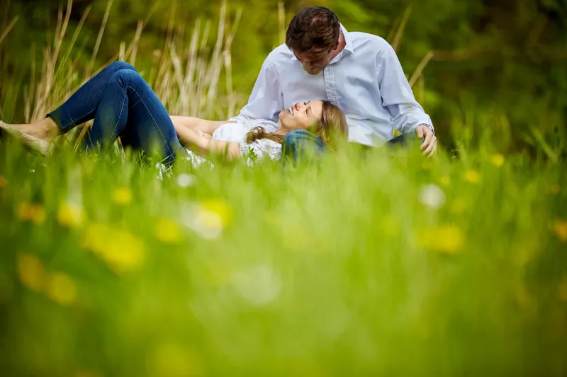 Een koppel in spijkerbroek en wit shirt ligt in het gras tussen gele bloemen