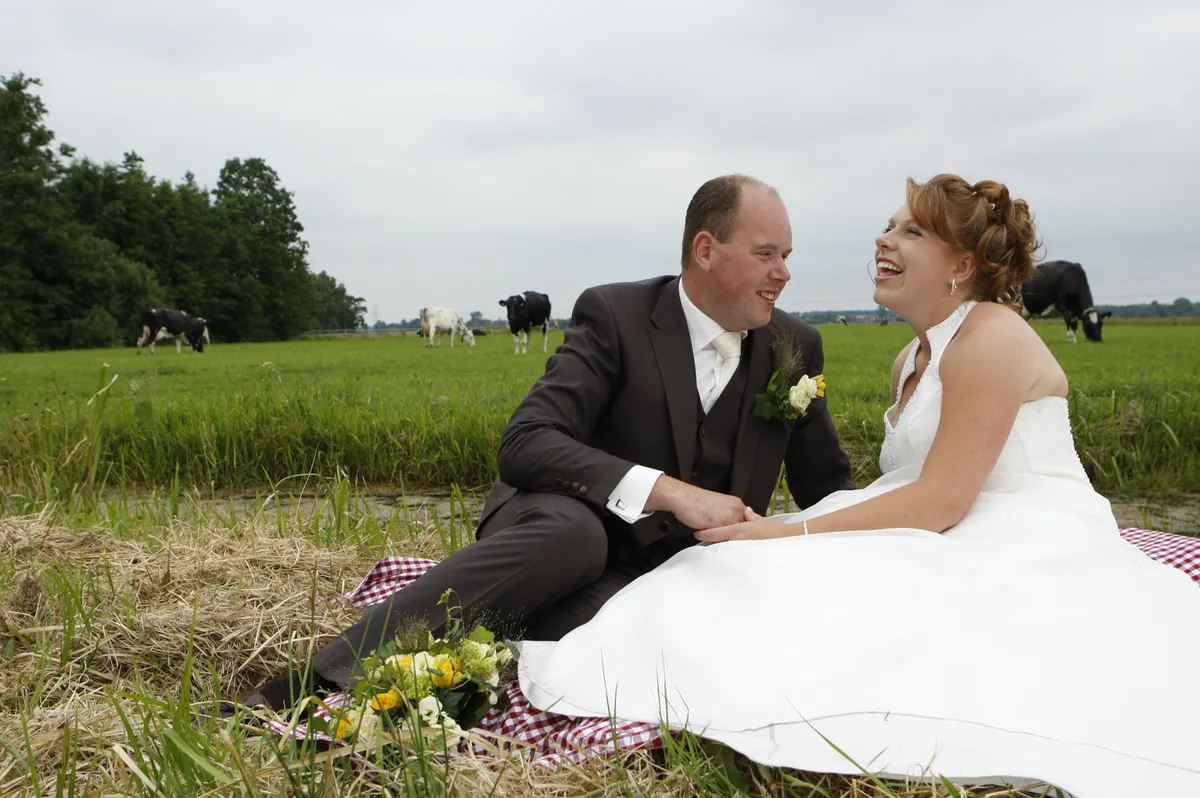 Yvonne en Robert-Jan zitten op een kleed in het weiland, de koeien erachter