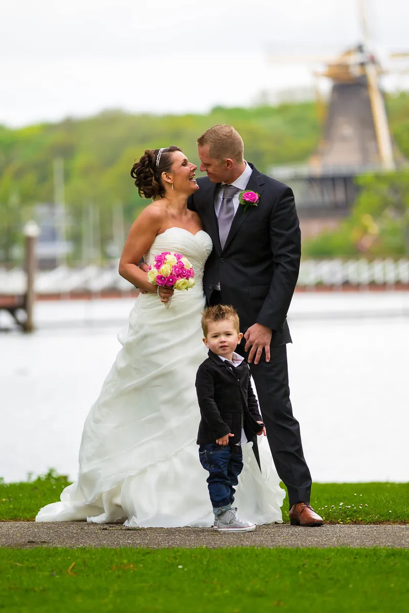 Michelle en Sven kussen aan het water, met de molen op de achtergrond en hun zoontje ernaast