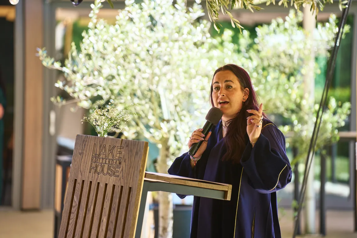 De trouwambtenaar spreekt bij het houten spreekgestoelte van Lake House, met een olijfboom erachter