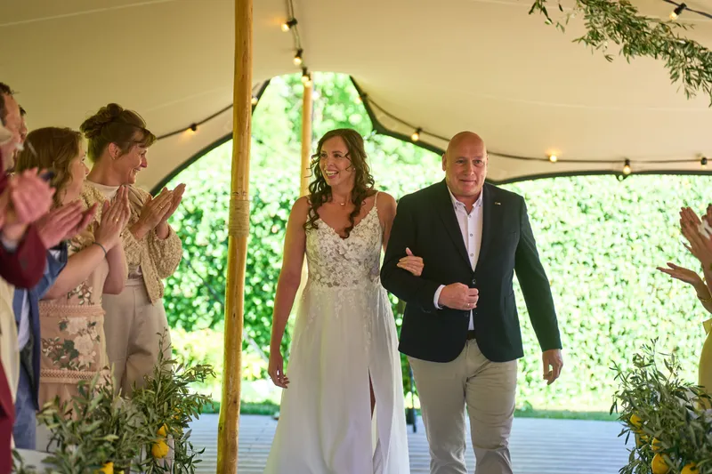 Michelle loopt arm in arm het gangpad op, tussen de klappende gasten